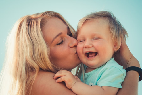 Photograph of a mother kissing her smiling toddler on the cheek