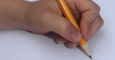 Yellow pencil grasped between the tips of the thumb, index and middle finger of a child's hand